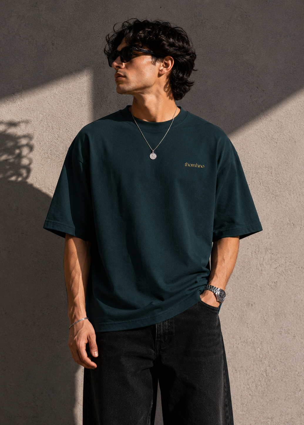 Man wearing a dark green t-shirt with a logo against a textured wall.