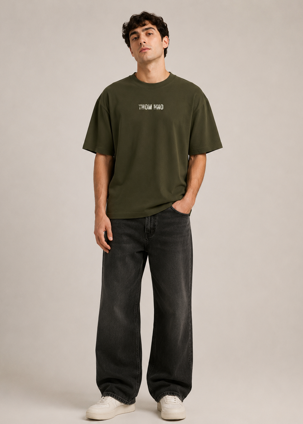 Man wearing an olive green t-shirt and black jeans against a plain background